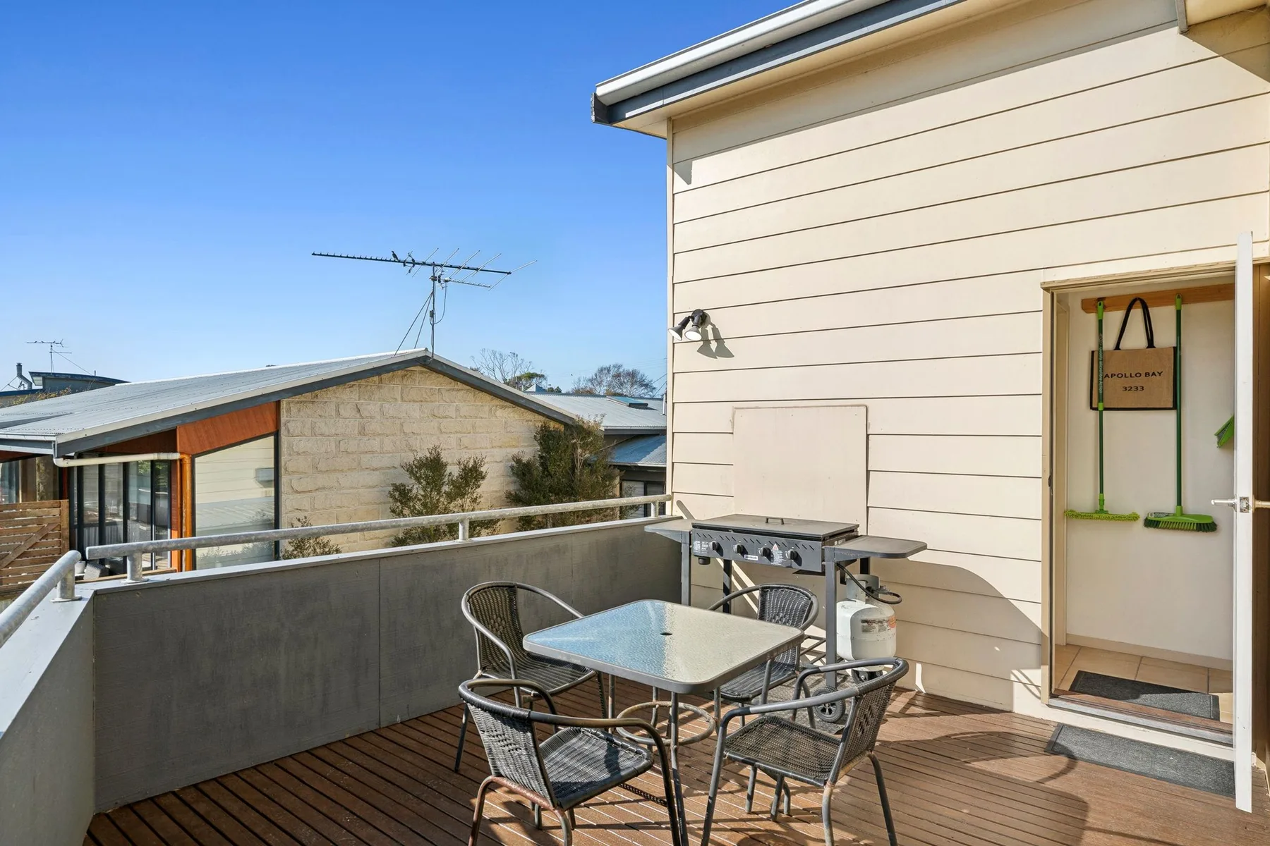 An outdoor deck has a dining table and seating beside a light-sided building.