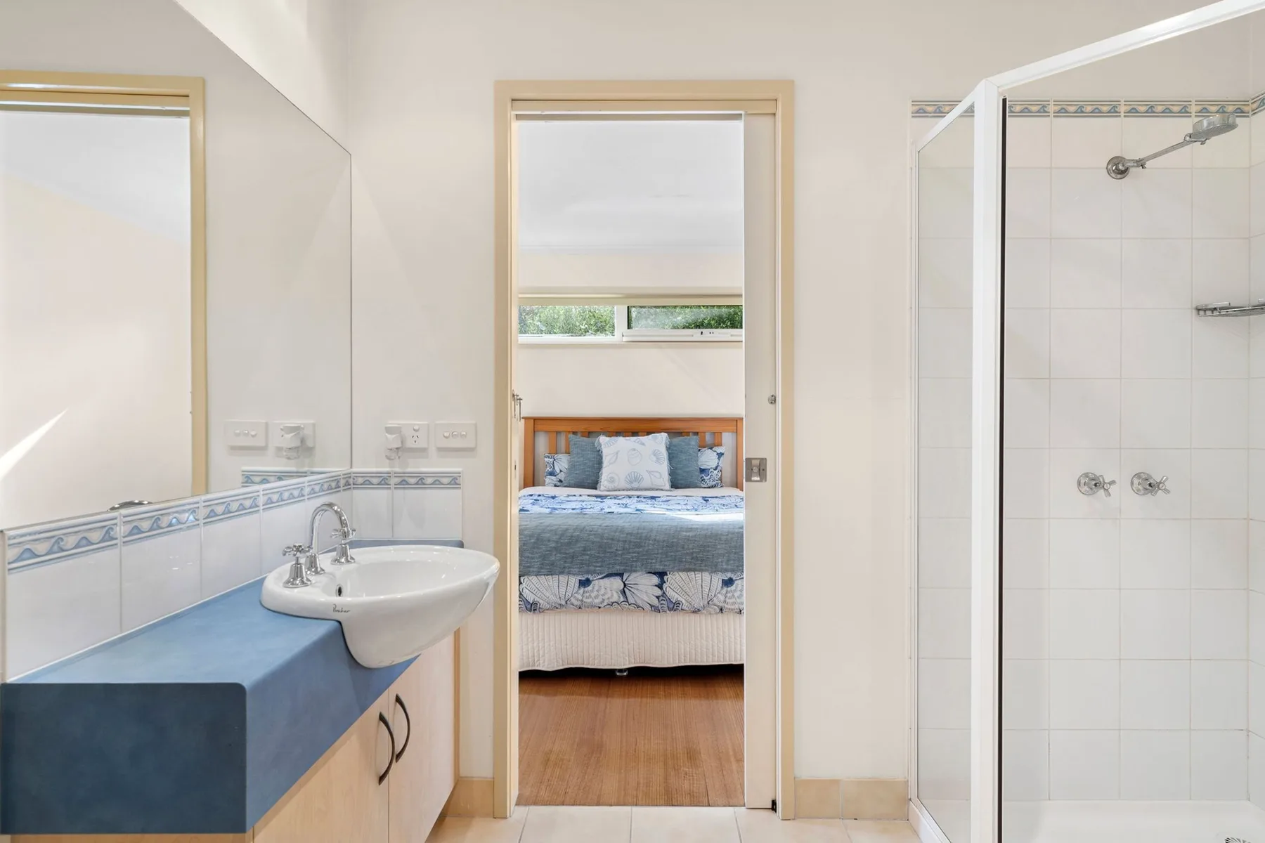 A bright bathroom opens onto a bedroom with a bed and window.