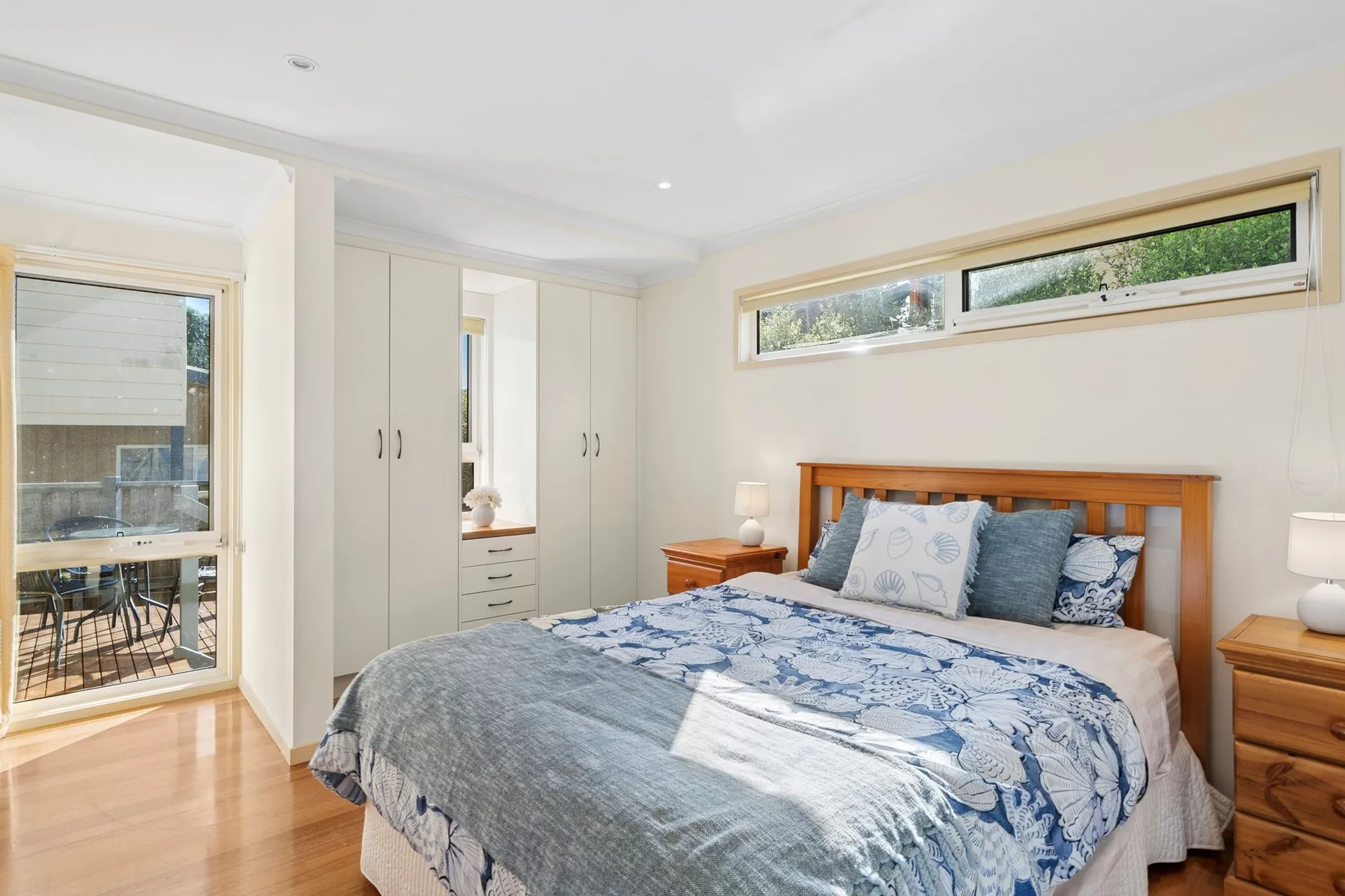 A bright bedroom with a wooden bed and large windows.