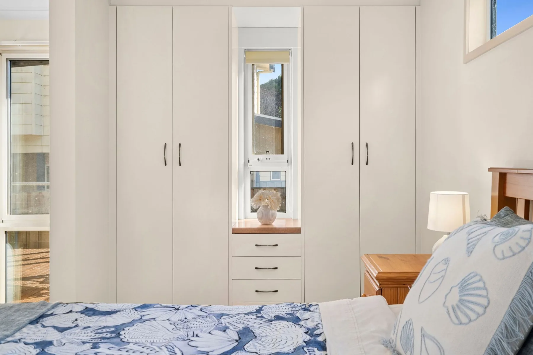 A bright bedroom with built-in wardrobes and a bed covered in blue patterned bedding.
