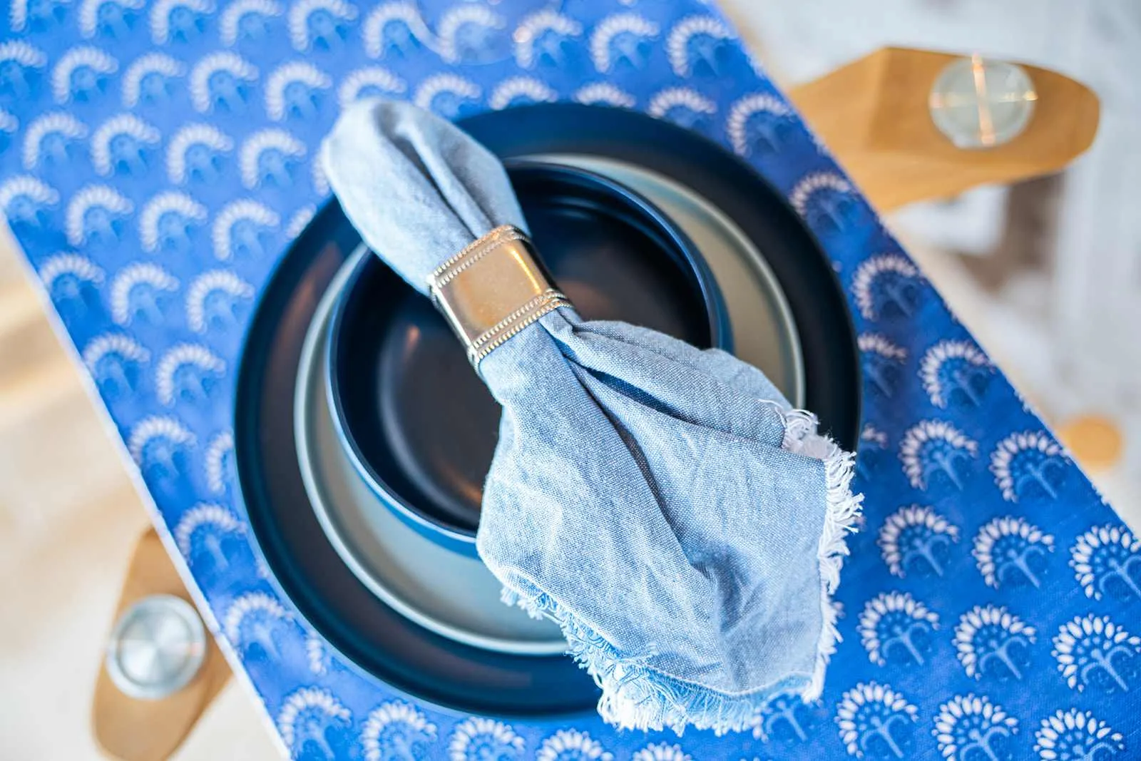 Un lugar en la mesa con un plato oscuro y una servilleta azul sobre un mantel estampado.