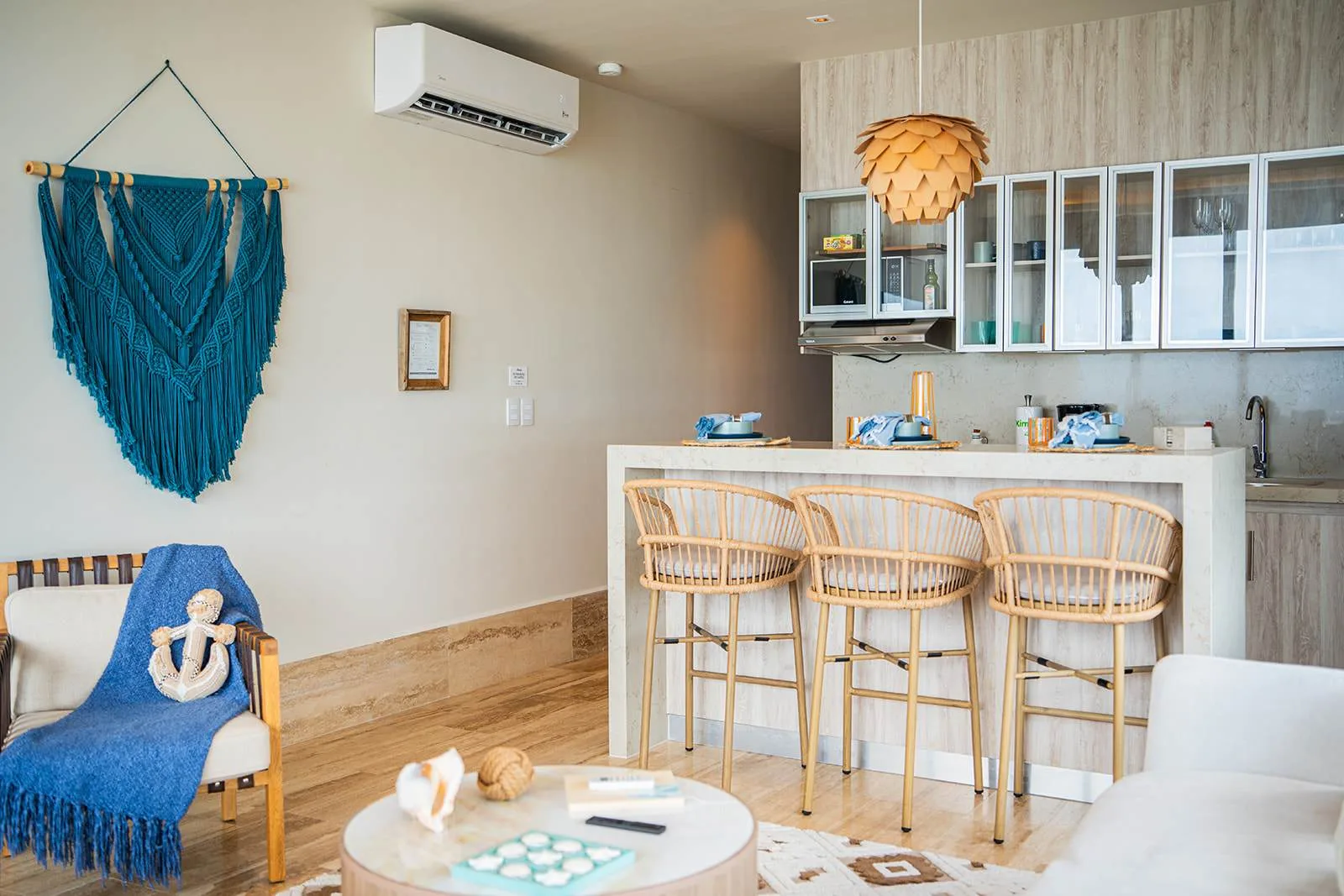 Una luminosa sala de estar abierta con barra de cocina y lámpara colgante tejida.