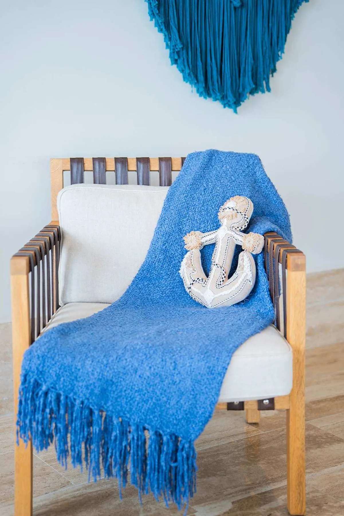 Un sillón de madera acolchado tiene una manta azul y un adorno de ancla.