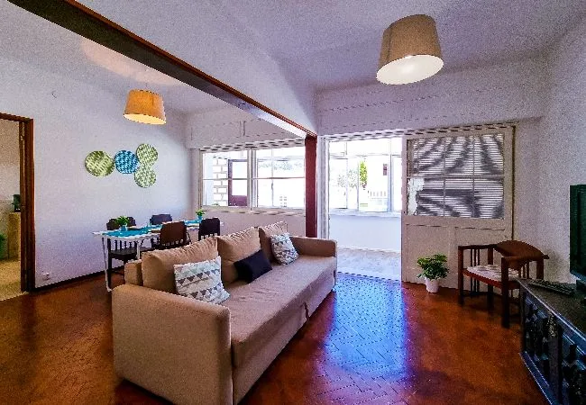 A living room with seating, a dining table, and large windows.