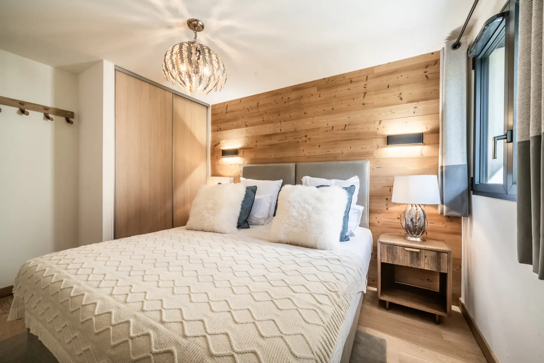 Un dormitorio con una cama bien tendida, una pared revestida de madera y una ventana.