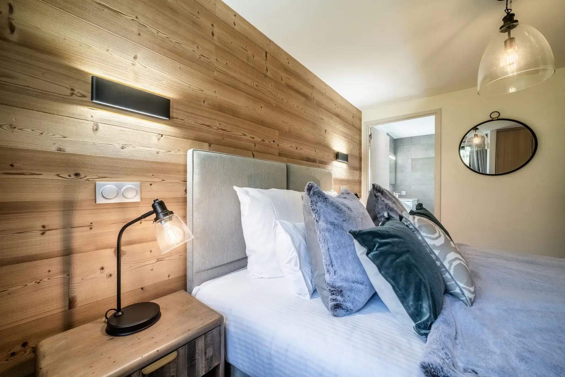 Un dormitorio con una cama vestida con ropa de cama blanca y azul junto a una pared revestida de madera.