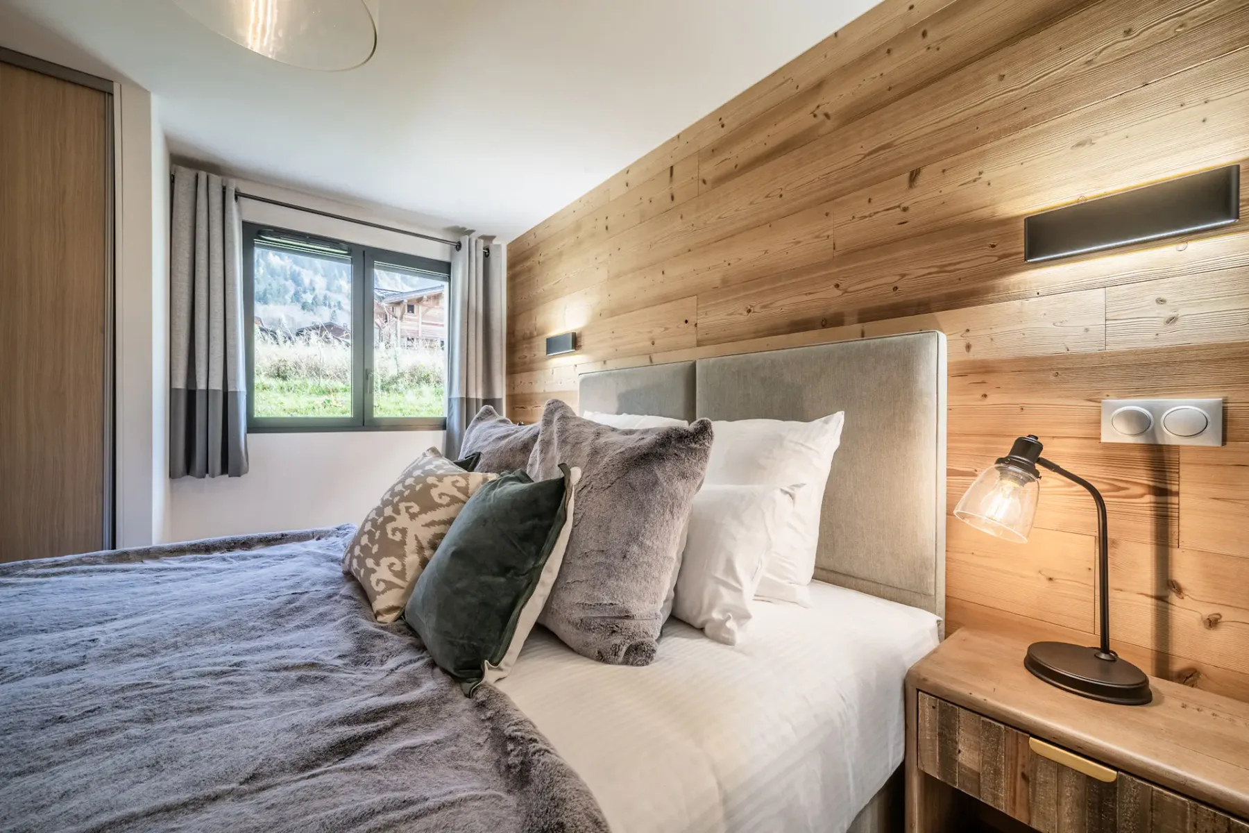 Un dormitorio con una cama junto a una pared revestida de madera y una ventana.