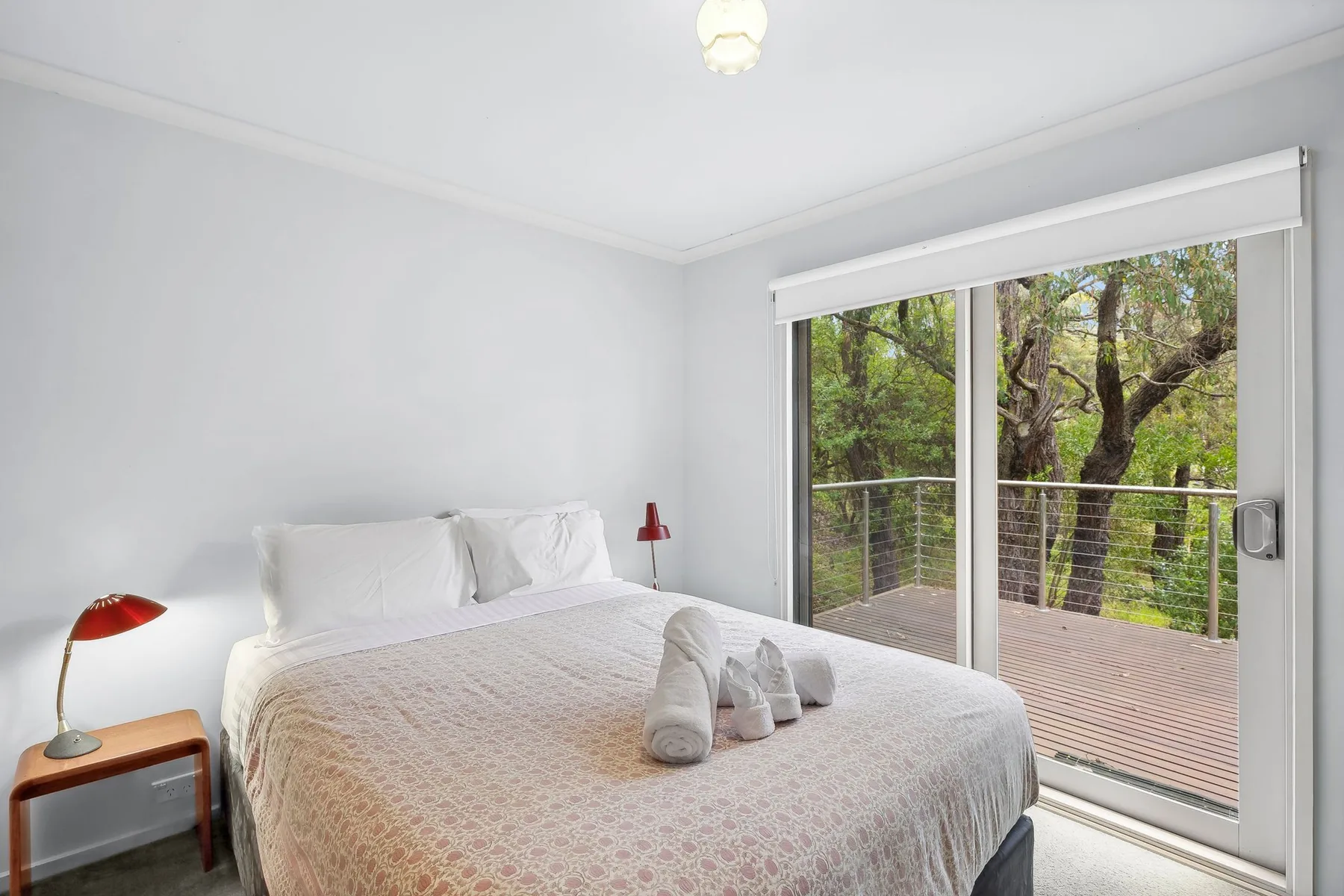 A bright bedroom with a bed beside large sliding glass doors overlooking trees.