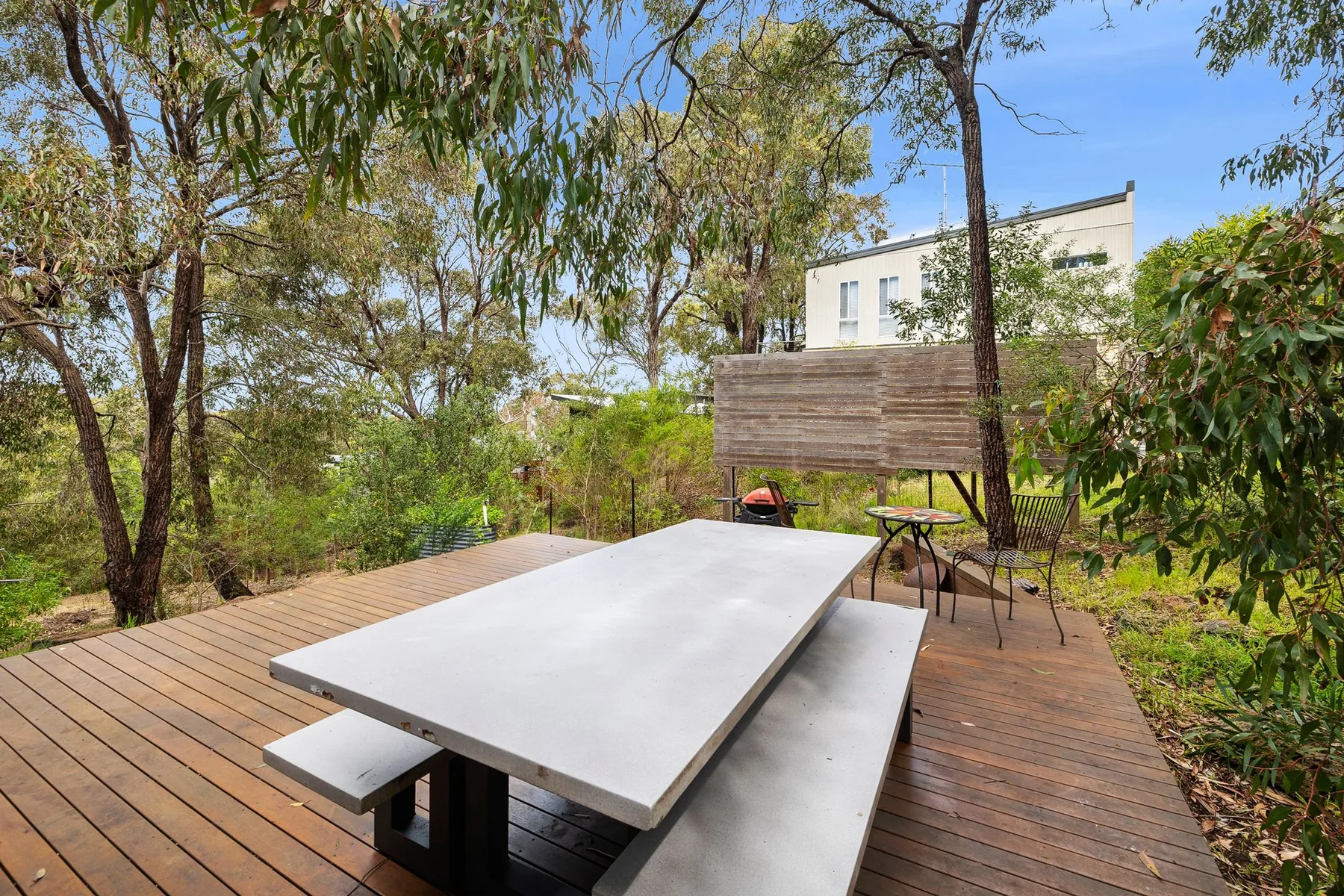 An outdoor dining area on a wooden deck is surrounded by leafy trees.