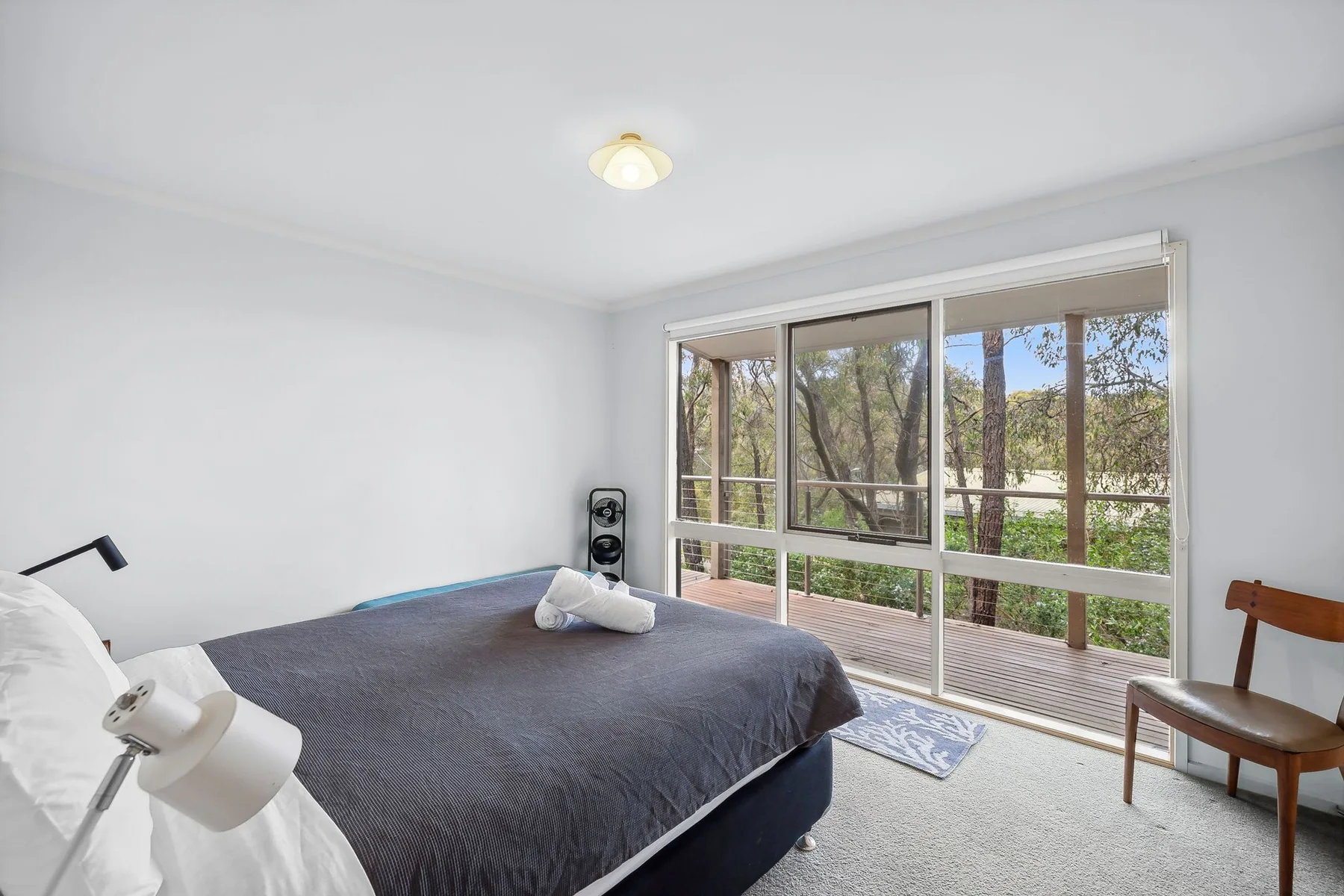 Bedroom with a large bed beside wide windows overlooking trees.