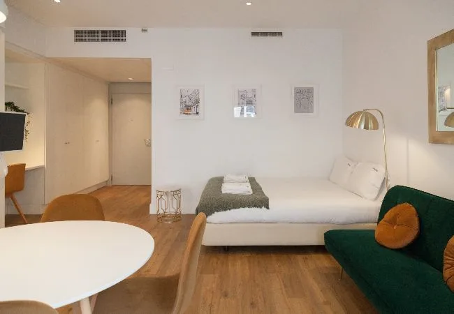 Un dormitorio luminoso con una cama blanca, un sofá verde y una mesa redonda.