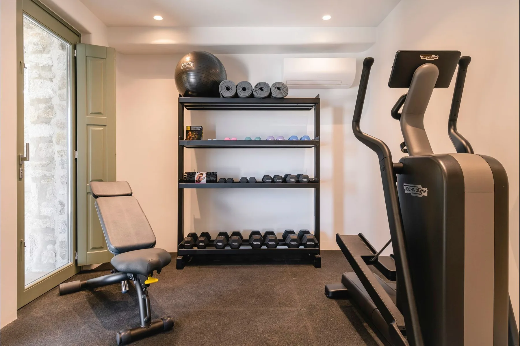 A home gym with weight racks, exercise equipment, and a large window.