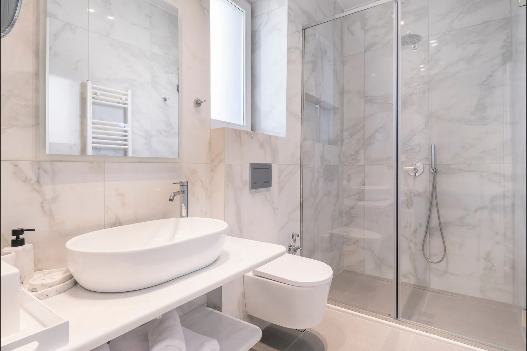 A marble bathroom with a vessel sink, wall-mounted toilet, and glass shower.