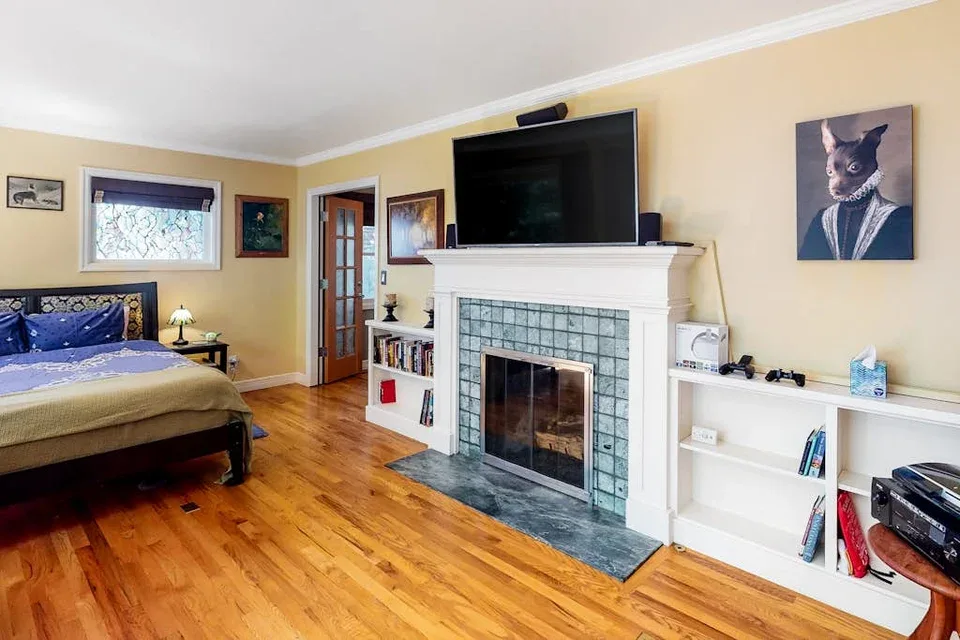 A bedroom with a bed, a fireplace, and a television above the mantel.