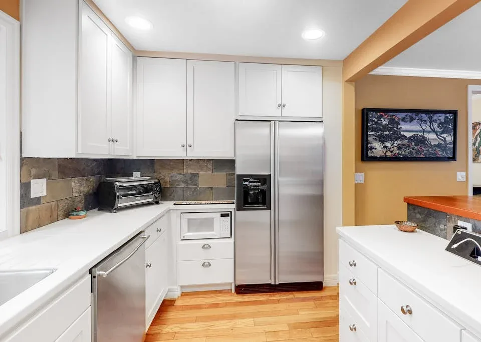 A bright kitchen with white cabinets, stainless steel appliances, and wood flooring.