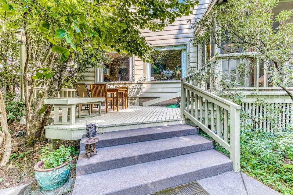 A raised outdoor deck with dining seating, stairs, and surrounding greenery.