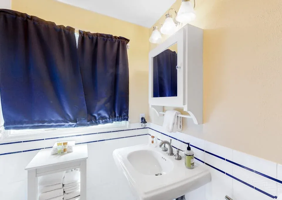 A bathroom vanity with a sink, mirror, and dark curtains over the window.