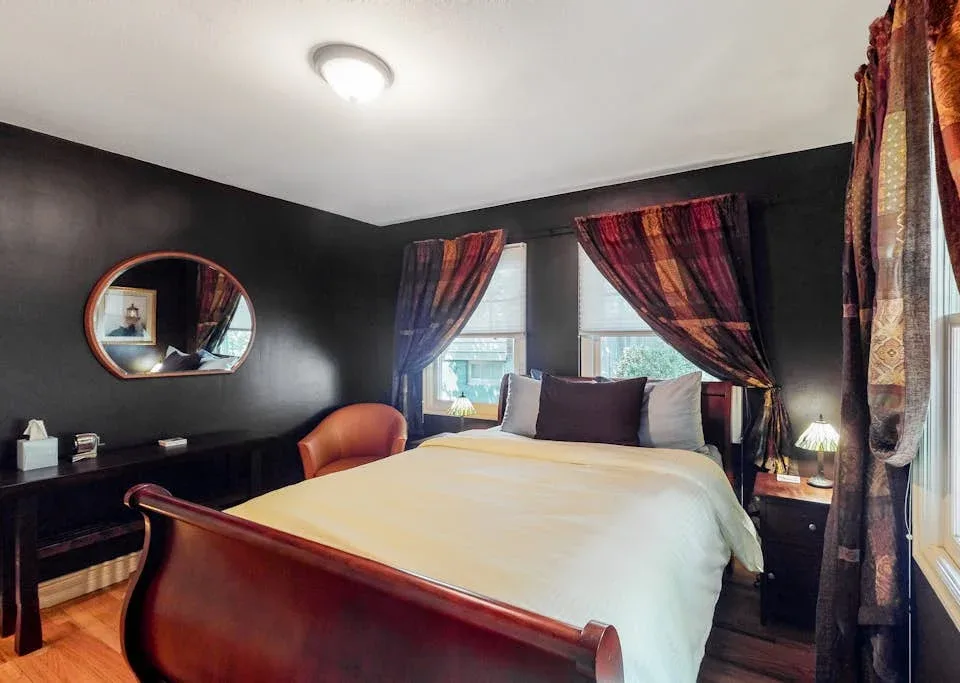 A bedroom with a large bed, dark walls, and colorful curtains.