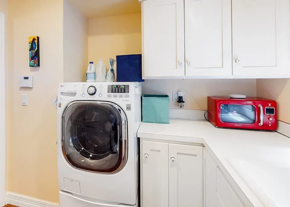 A laundry area with a front-loading washing machine beneath white cabinets.