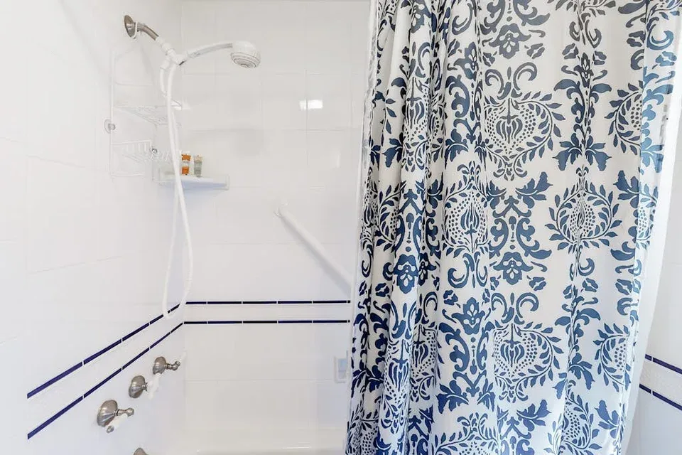 A tiled bathroom with a shower and a patterned curtain.