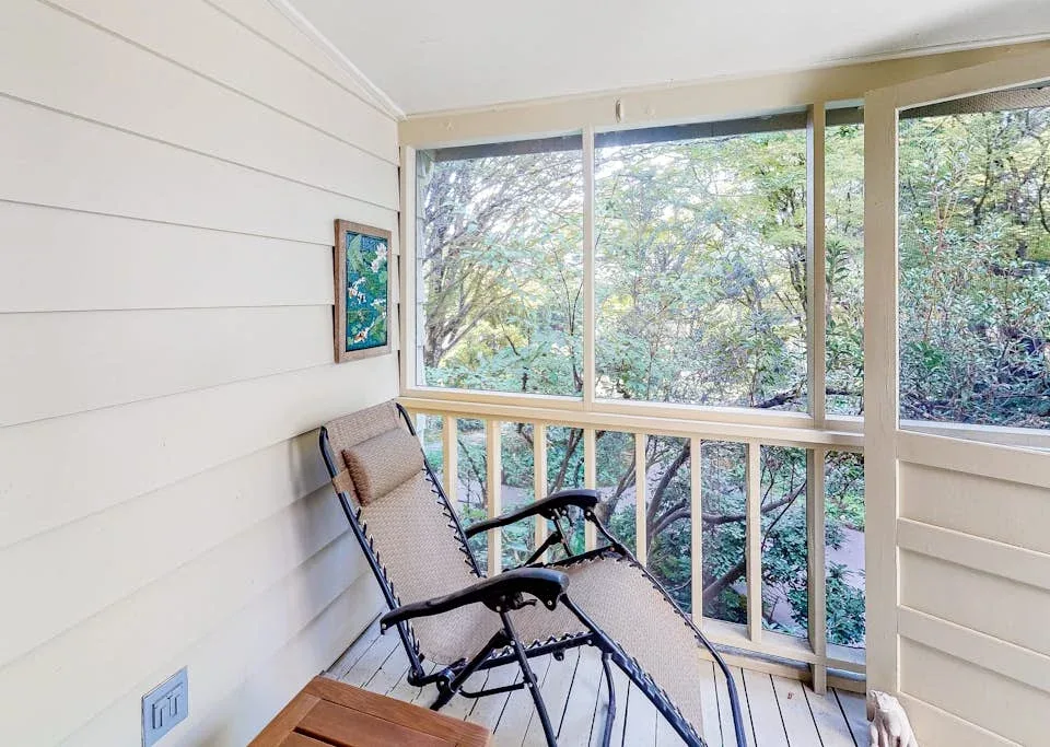 A porch seating area overlooks leafy trees through large windows.