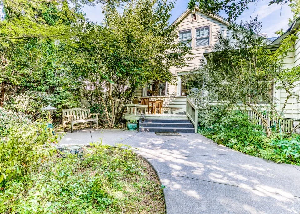 A garden path leads to a raised deck beside a light-colored house.