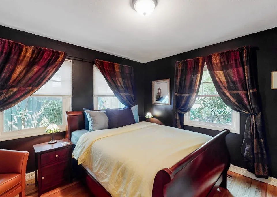 A bedroom with a bed, dark walls, and colorful curtains around the windows.