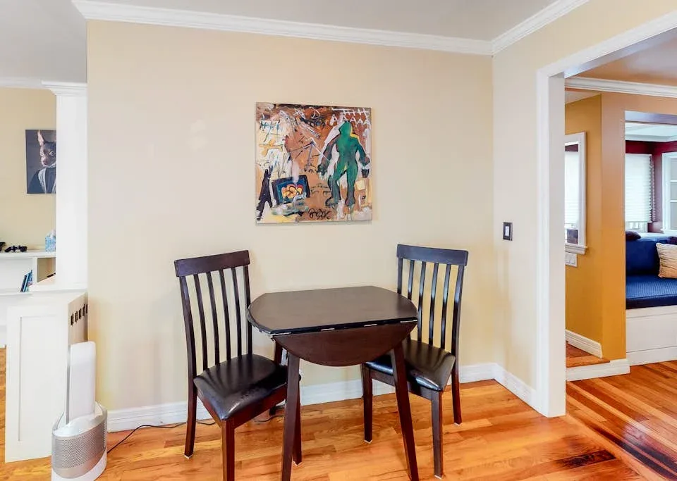 A dining area with a dark table and chairs beneath a colorful painting.