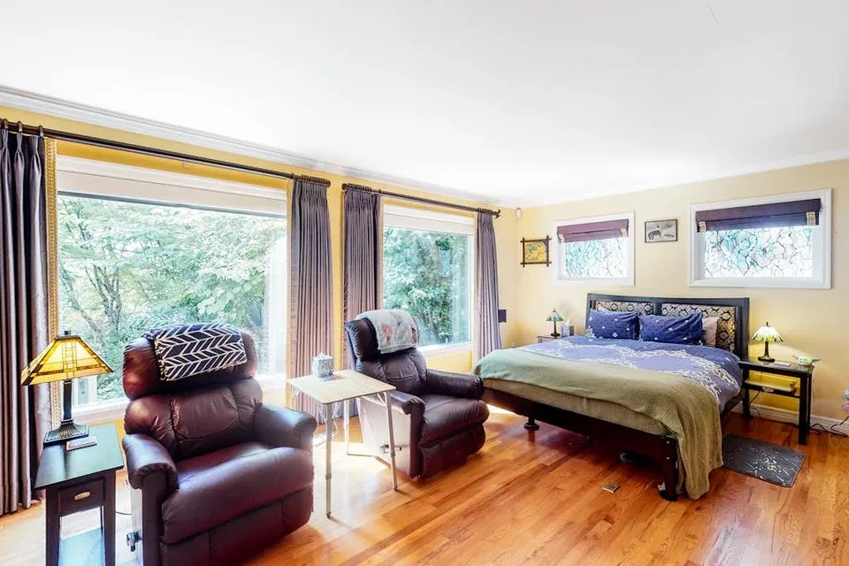 A bedroom with a bed, seating, and large windows overlooking trees.