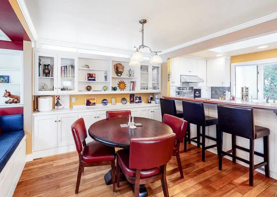 A dining area with a round table and red chairs beside a kitchen island.