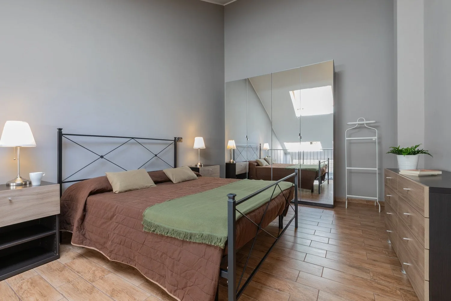 A bedroom with a metal-framed bed, bedside lamps, and a large mirror.