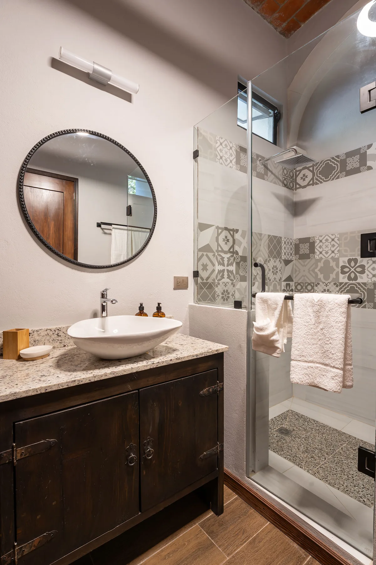 A bathroom with a sink vanity and a glass shower with patterned tile.