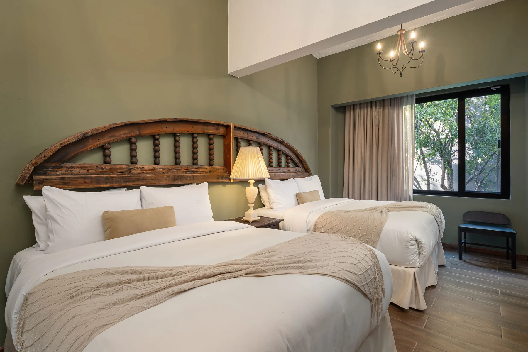 A bedroom with two beds, a bedside lamp, and a window overlooking trees.