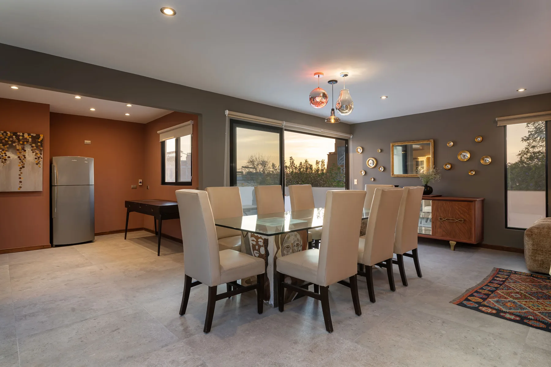 A dining area with a glass table and upholstered seating beside large windows.