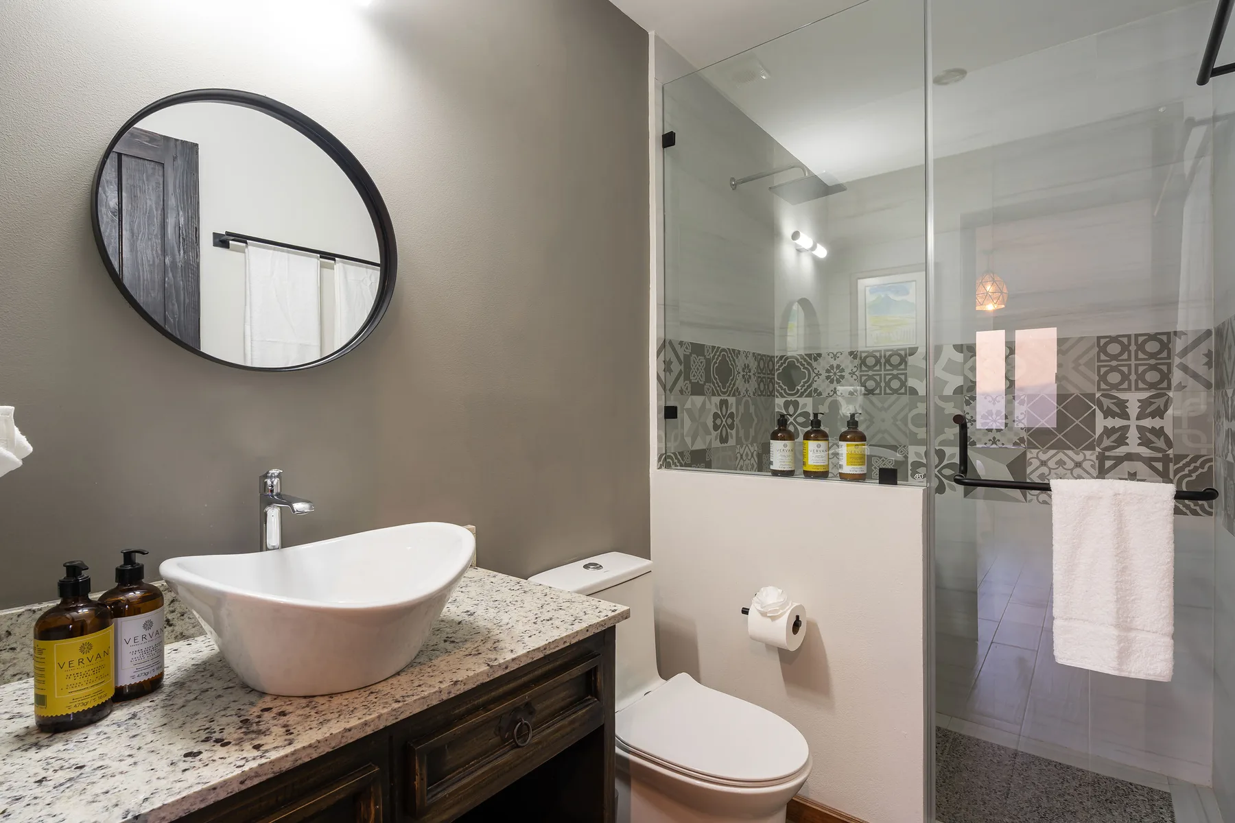 A bathroom with a vessel sink, toilet, and glass shower.