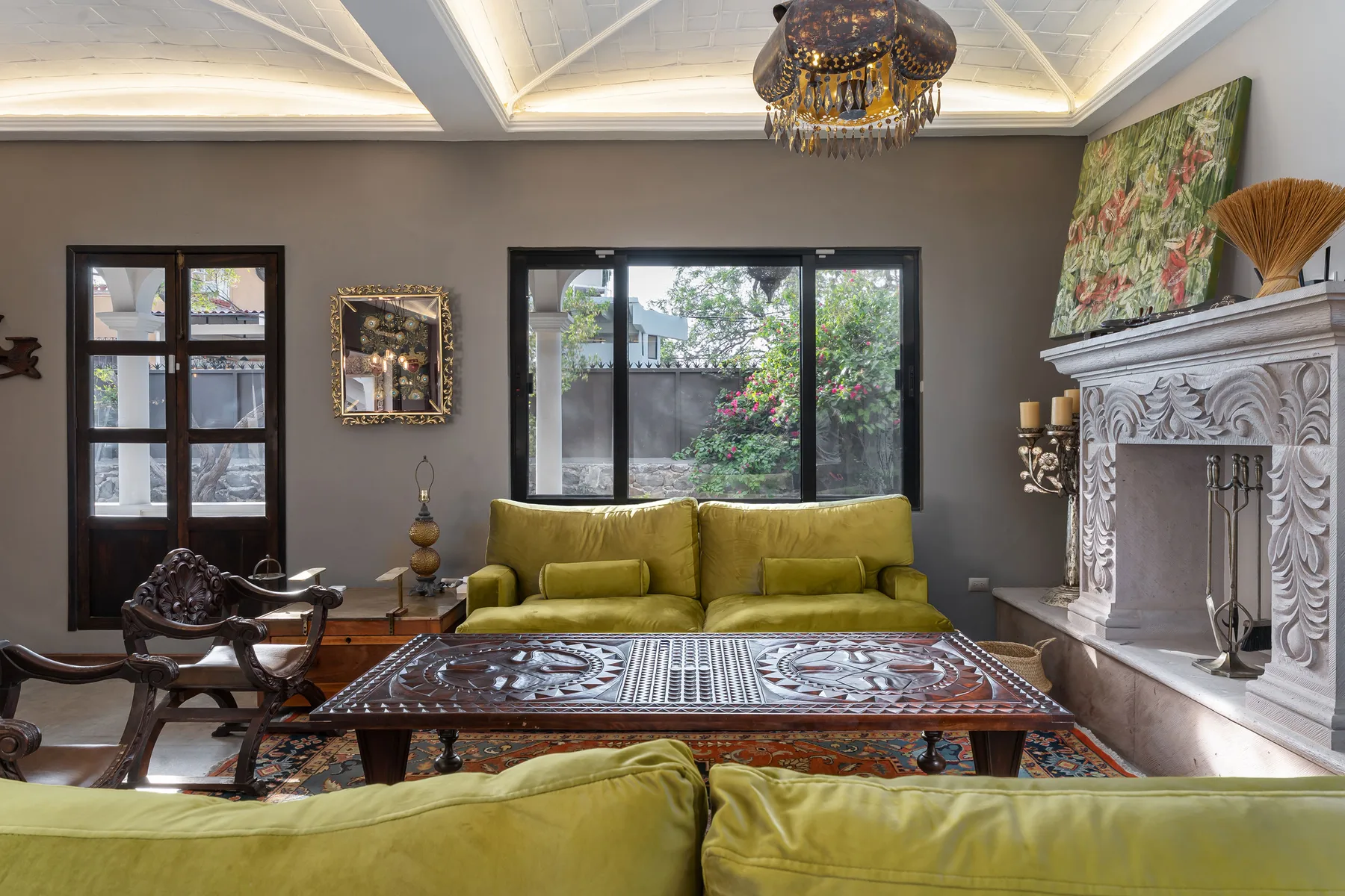 A living room with green seating, a carved coffee table, and a large decorative fireplace.