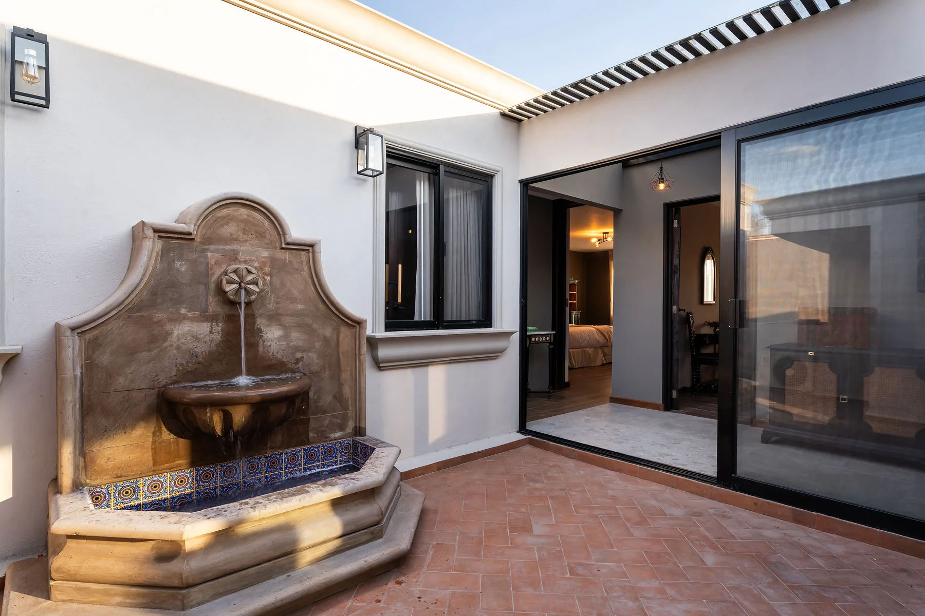 A tiled courtyard features a decorative wall fountain beside open doorways.