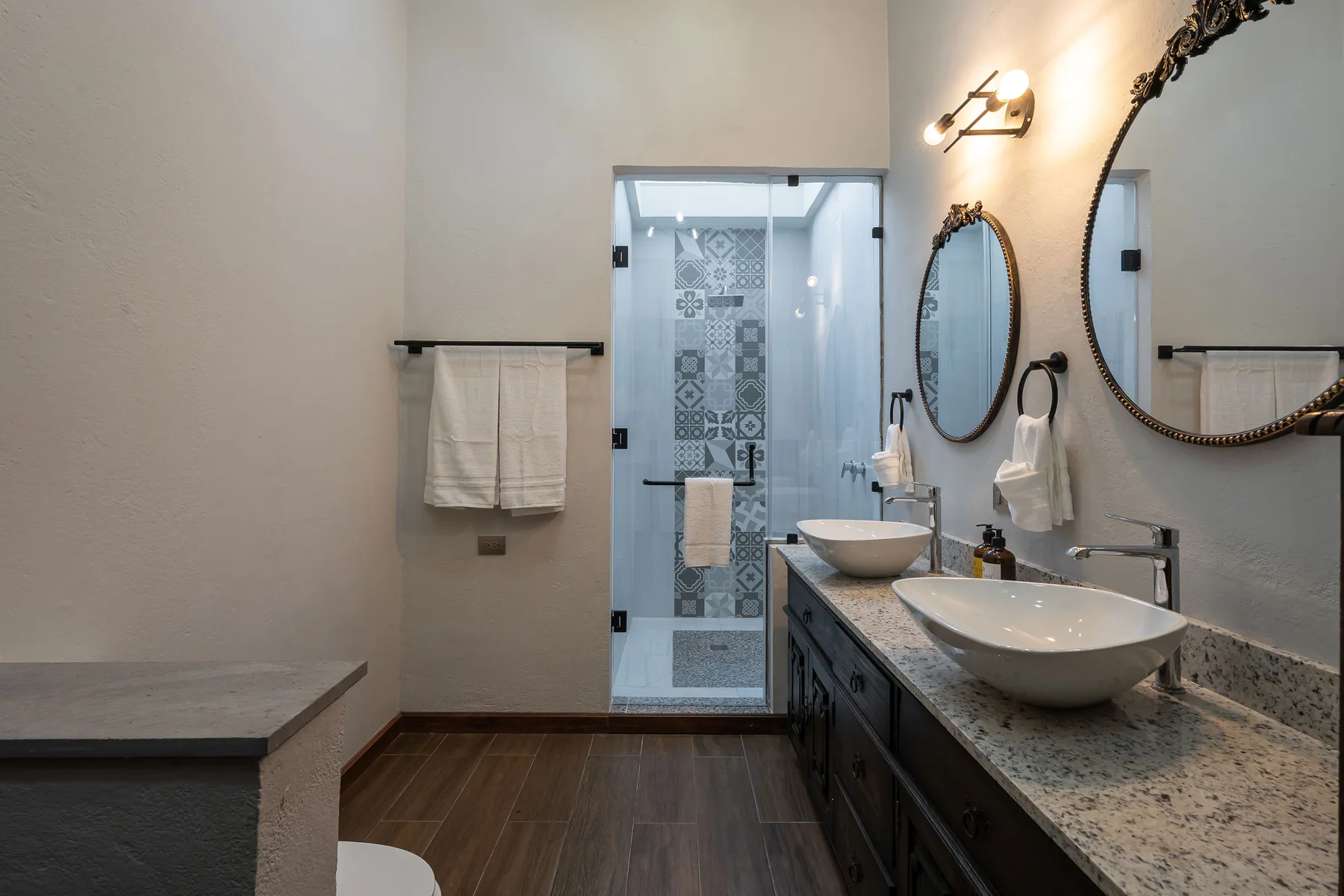 A bathroom with a glass shower, twin sinks, and wall mirrors.