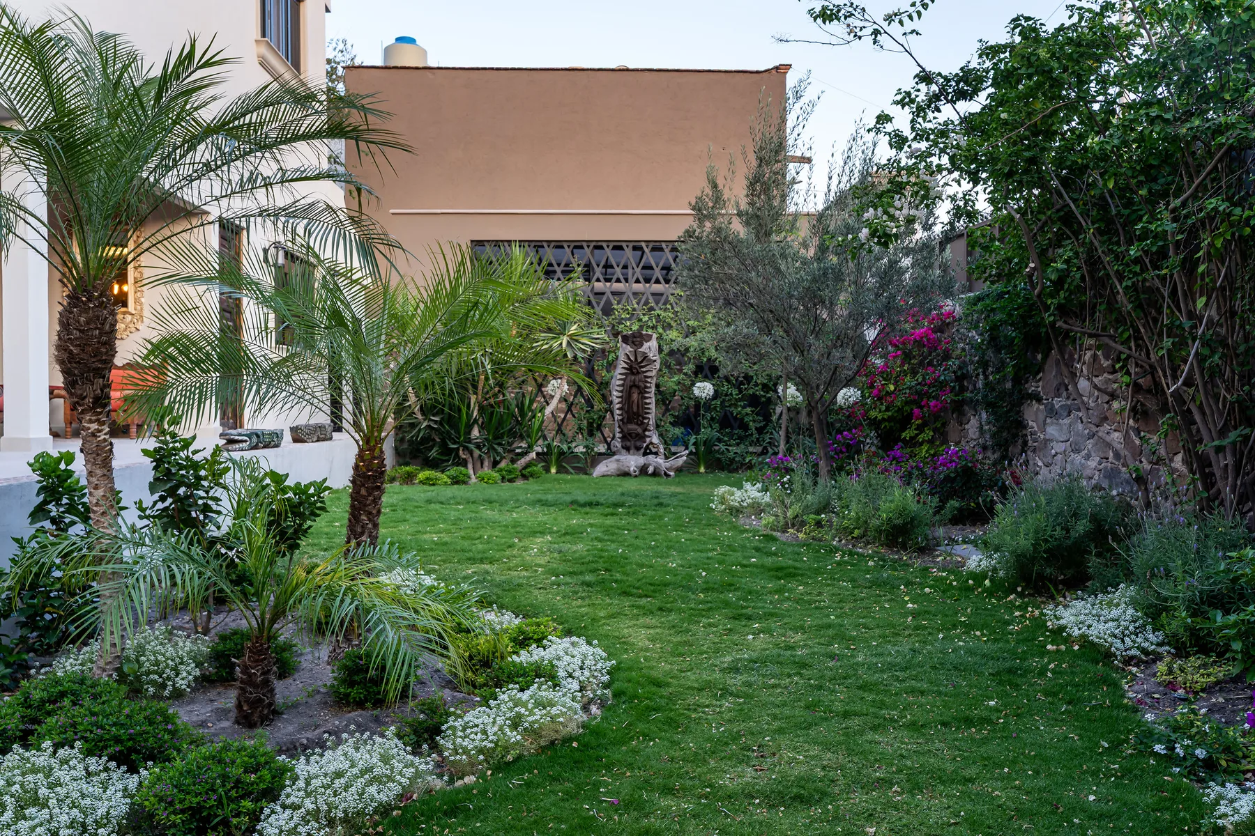 A landscaped garden with a lawn, palm trees, and flowering shrubs.