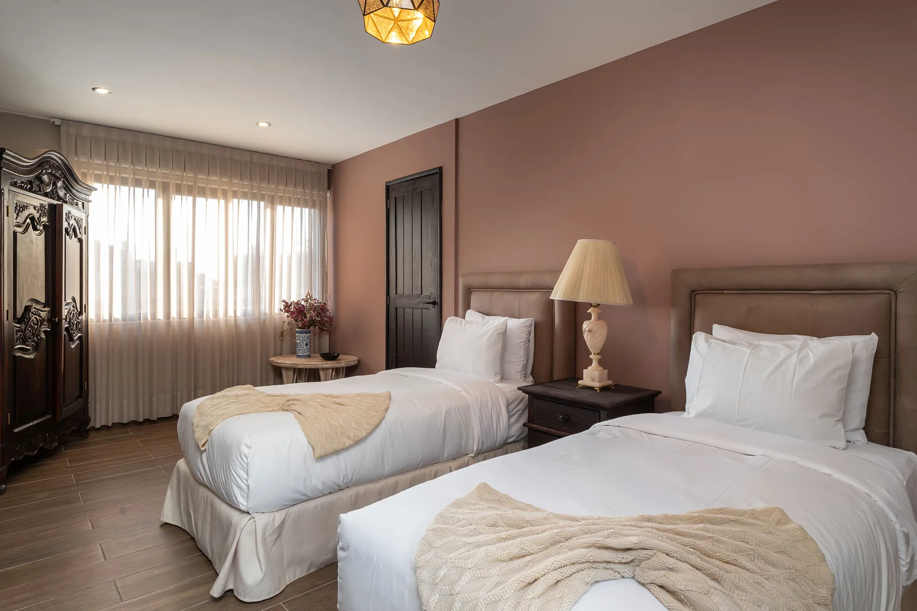 A bedroom with two beds, a bedside table, and a large curtained window.