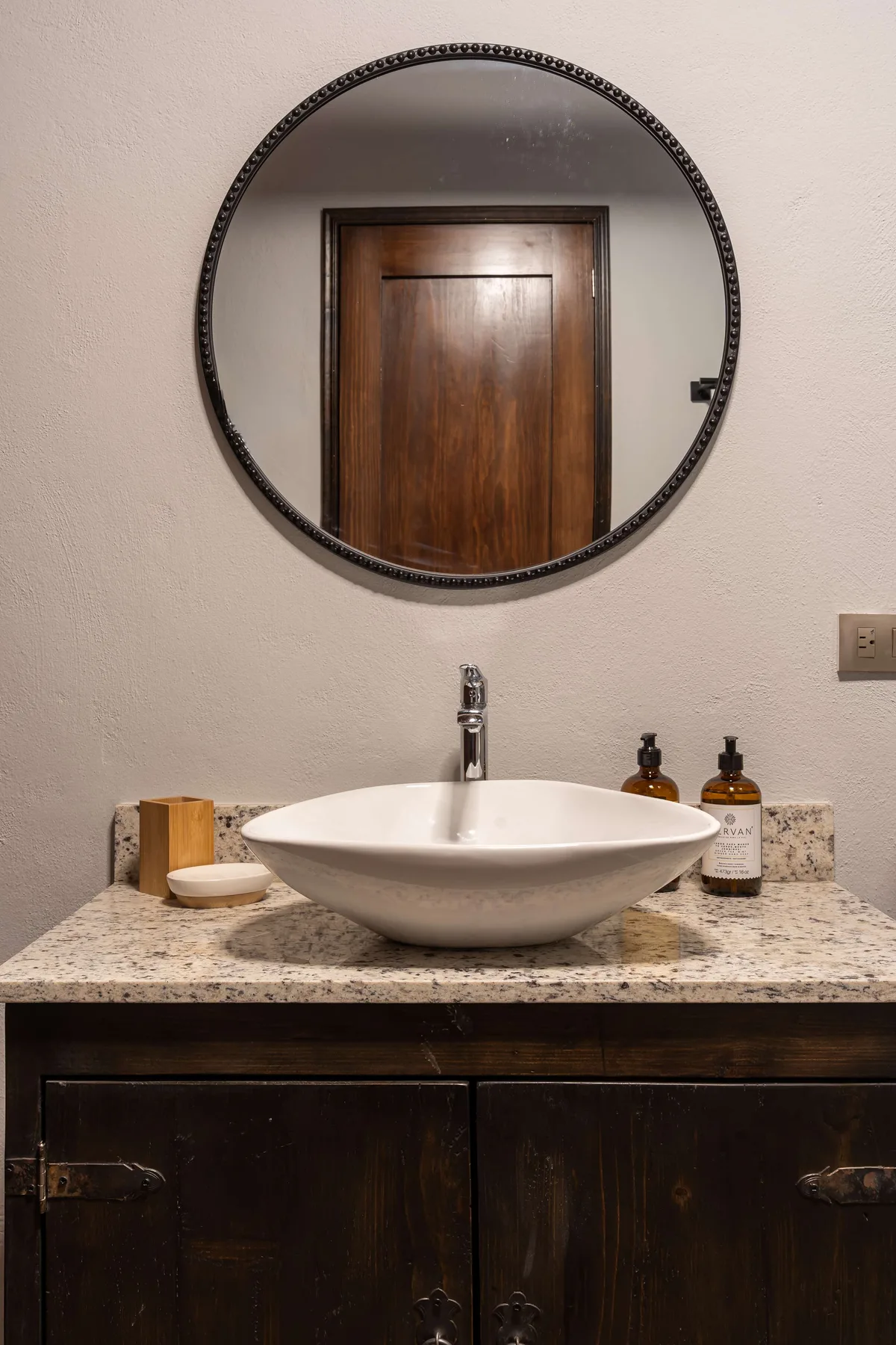 A bathroom vanity with a white vessel sink and round wall mirror.