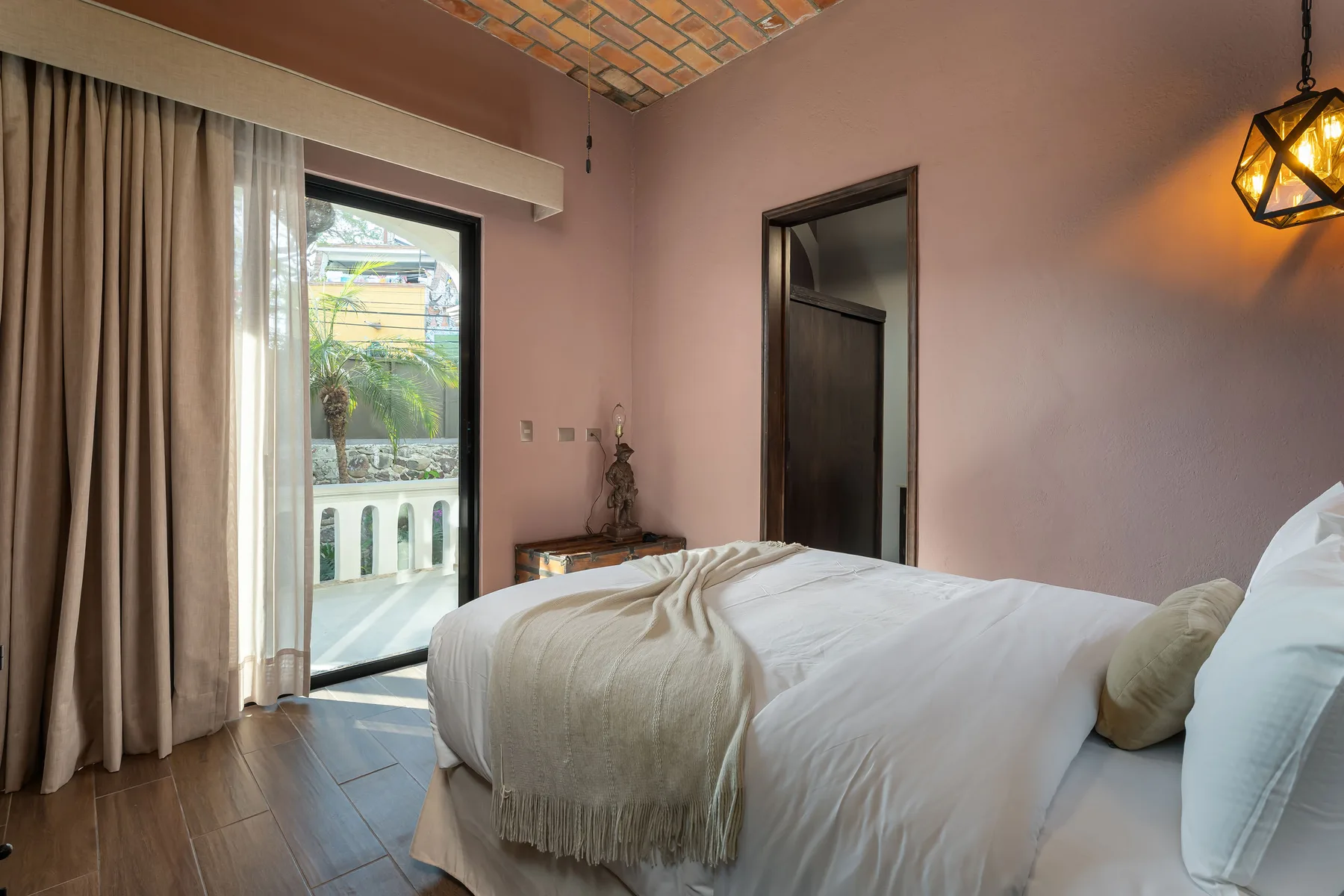 A bedroom with a neatly made bed beside a glass door and curtains.