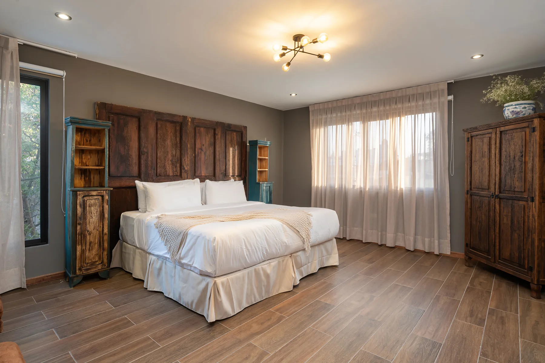 A bedroom with a large bed, wooden furnishings, and sheer curtains over the window.