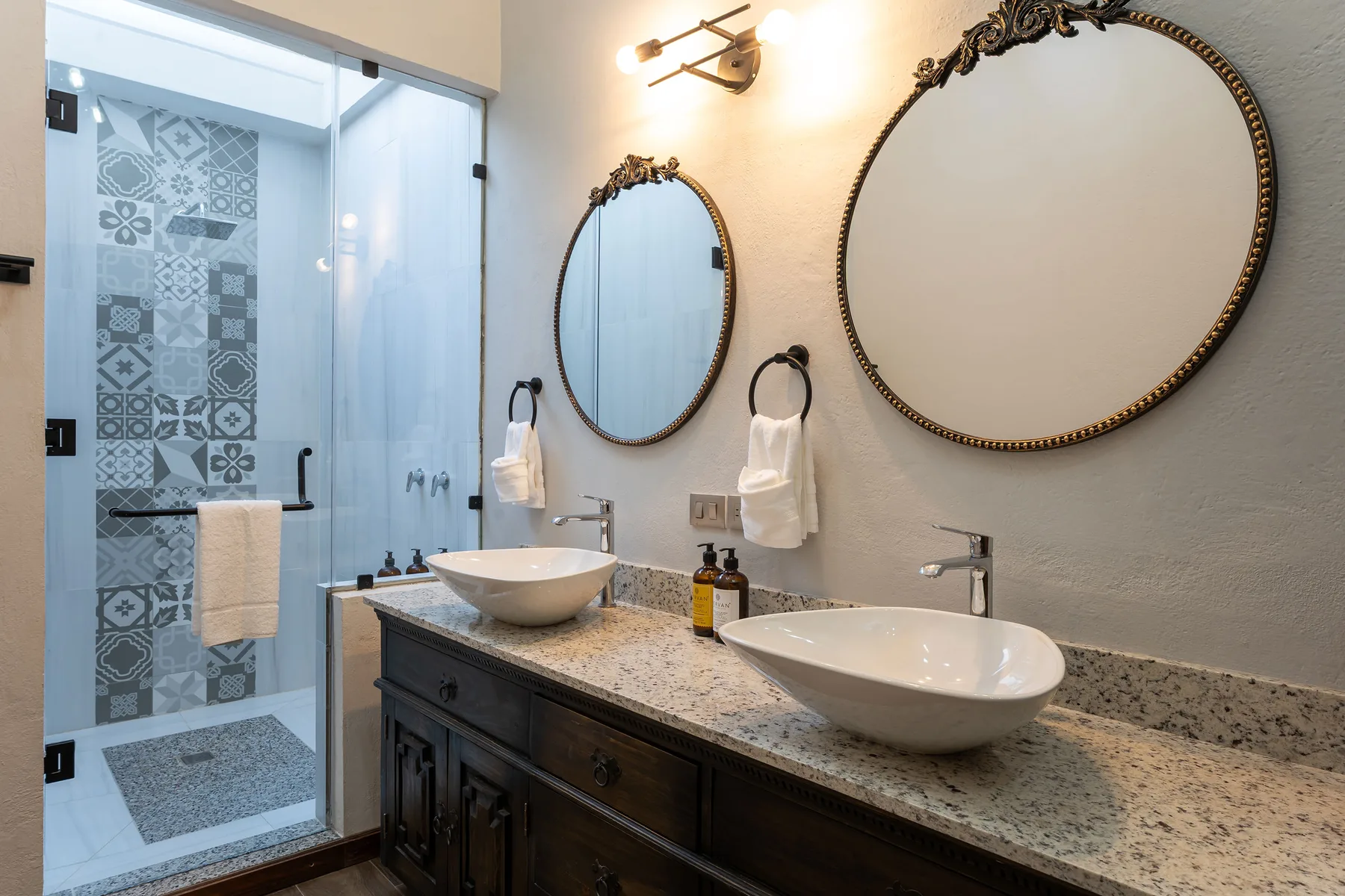 A bathroom vanity with two sinks and decorative mirrors beside a glass shower.