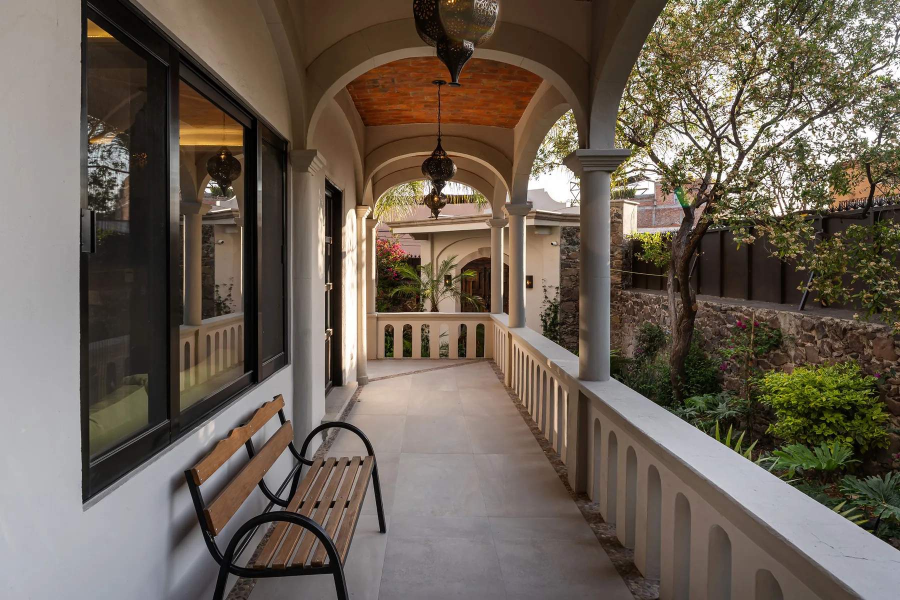A covered veranda with arched openings, a bench, and views of a courtyard garden.