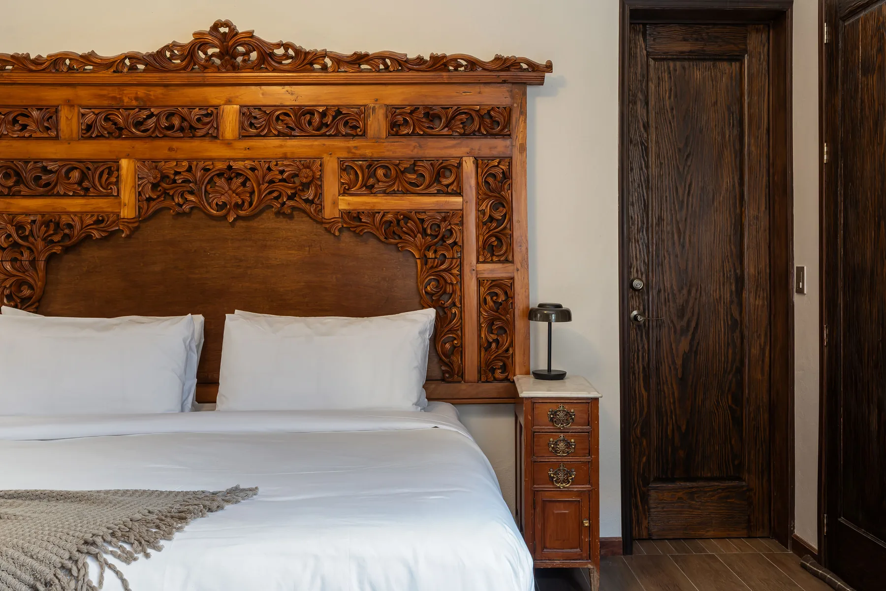 A bedroom with a white bed beneath an ornate carved wooden headboard.