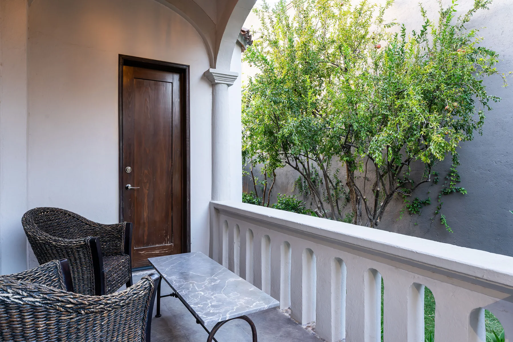A covered outdoor seating area overlooks leafy trees beyond a white balustrade.