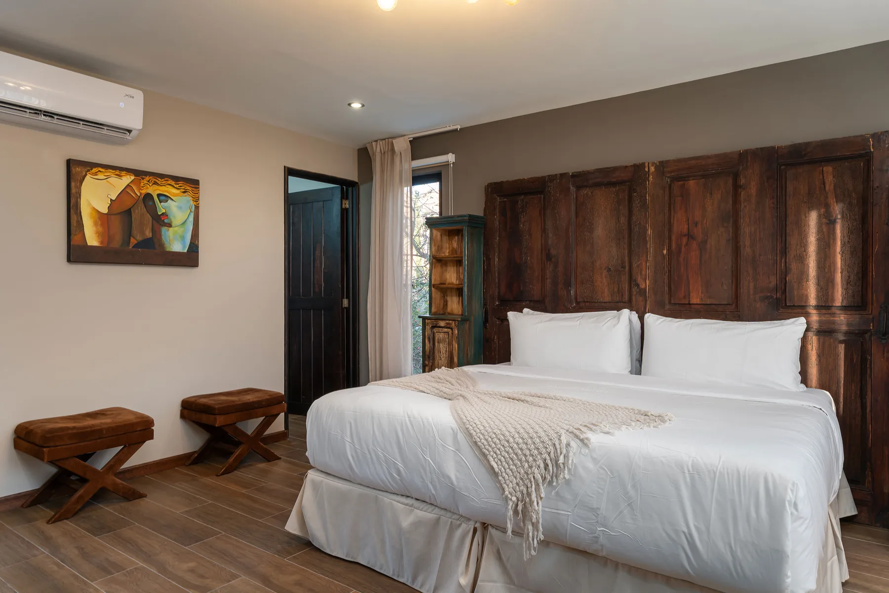 A bedroom with a white bed, dark wood headboard, and wall-mounted air conditioner.