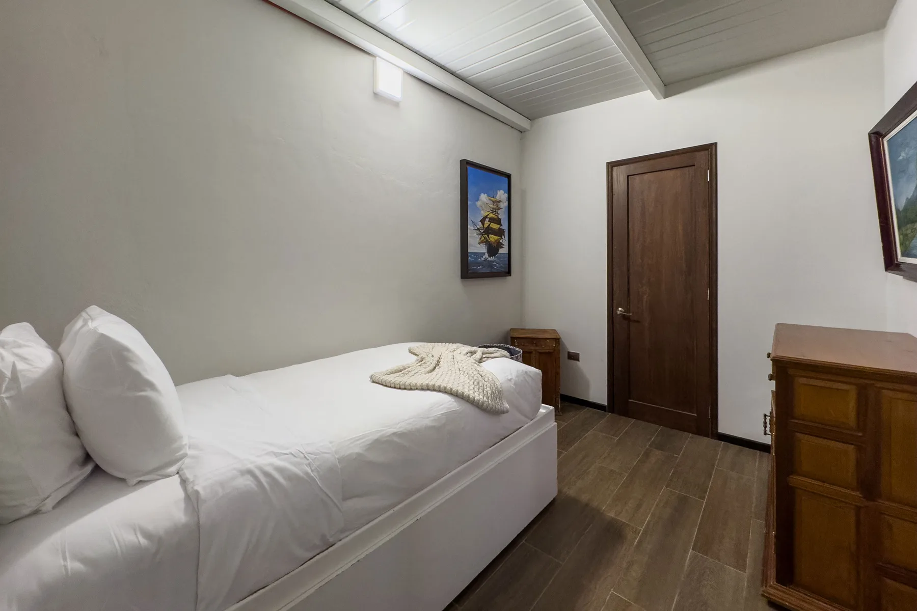 A bedroom with a single bed, wooden door, and dresser.