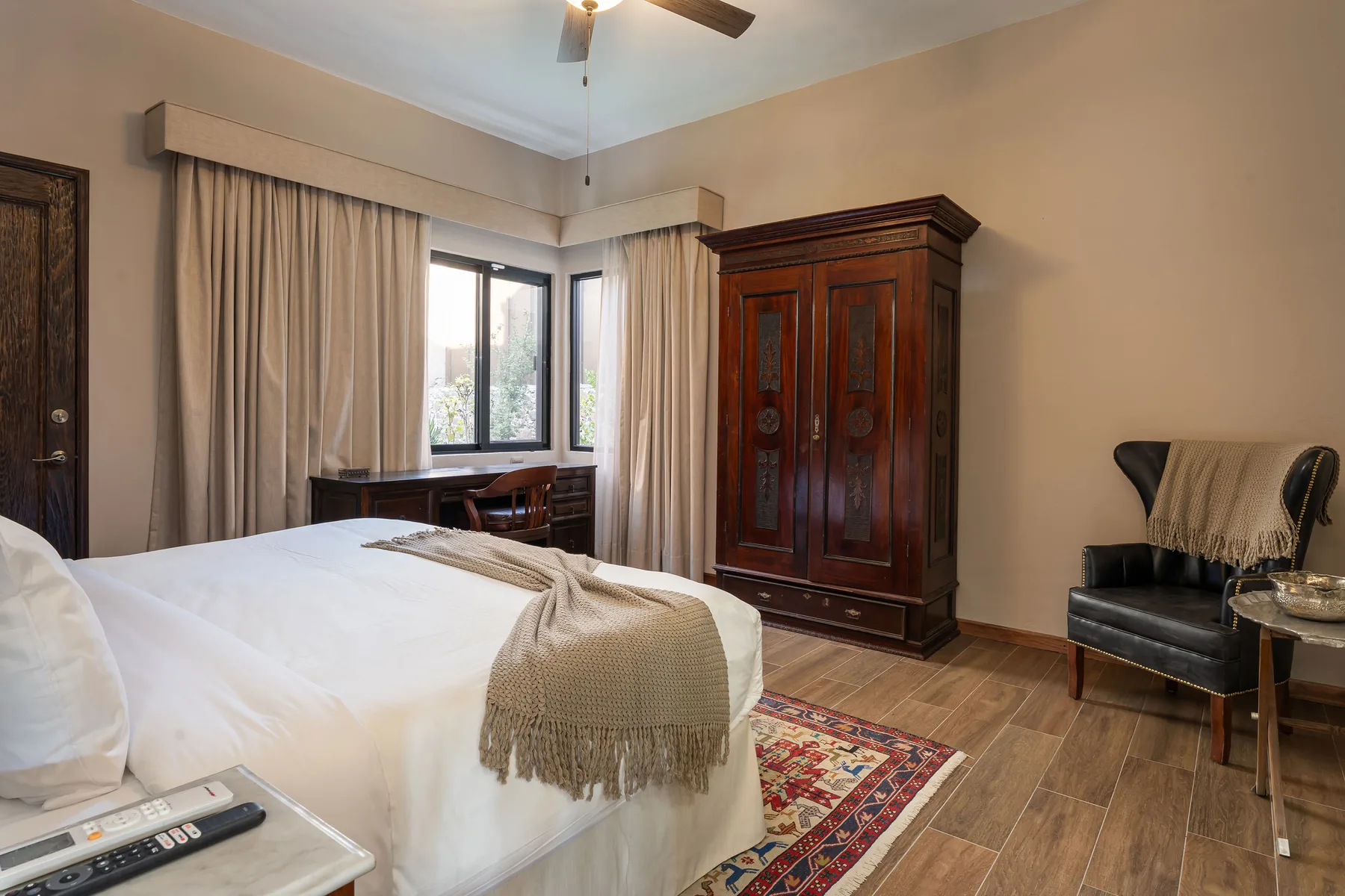 A bedroom with a bed, wooden wardrobe, and windows framed by curtains.